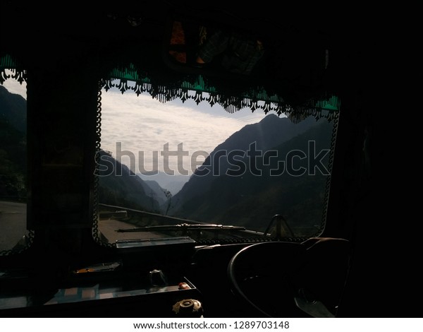 Snowy peaks, mountains, forest, highway\
and cloudy sky through the fuel truck windscreen. Himalayas.\
Kingdom  of Ladakh. State Jammu and Kashmir,\
India.