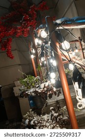 Snowy railing with string lights and winter plants. Festive winter night with glowing bulbs and snow covered plants creating a magical outdoor ambiance.