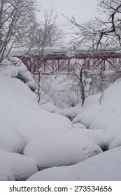 A Snowy River Scene With A Red Bridge Over Onsen Water In Niseko, Hokkaido, Japan