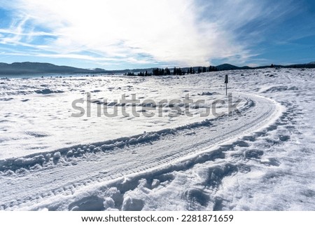 Snowy road with blue sky in the background the peaks of the mountains of the Asiago plateau and the woods of the Piana di Marcesina with small alpine huts in Marcesina Enego Vicenza Veneto Italy