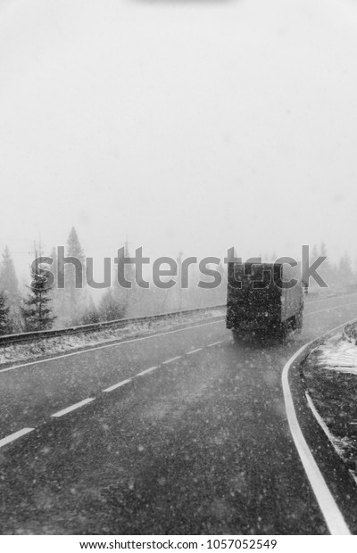 Snowy road, on the sides of trees, heavy snow. The\
concept of the problems of the road situation of transportation,\
increased risk, cleaning roads. truck and cars, vertical, black and\
white