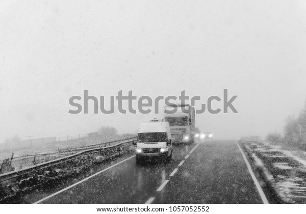 Snowy road, on the sides of trees, heavy snow. The\
concept of the problems of the road situation of transportation,\
increased risk, cleaning roads. on the road truck and cars, black\
and white