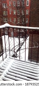 Snowy View Of A Fire Escape And Back Alley With Red Brick Buildings Surrounding The Alleyway In New York City.