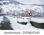 A snowy waterfront with a cleared path, highlighting the challenges faced by municipal workers during winter. A road work sign in the foreground underscores their ongoing efforts amidst harsh