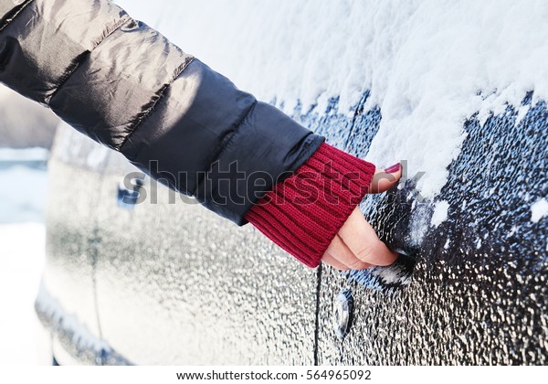 Snowy winter in a city on a sunny day. Car after\
snowfall in the parking lot. Young woman trying to open the icy\
car\
                              \
