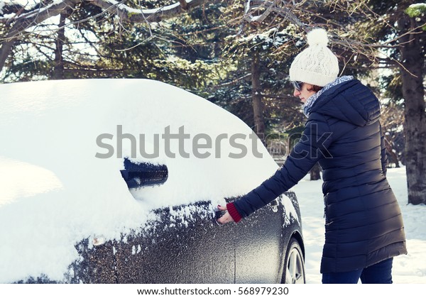 Snowy winter in a city on a sunny day. Car after\
snowfall in the parking lot. Young woman trying to open the icy\
car\
                              \
