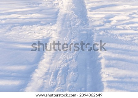 Snowy winter pathway with shoes prints. Human feet traces in the snow. Snow footway with feet prints. Hiking, local travel or staycation concept. Horizontal format.