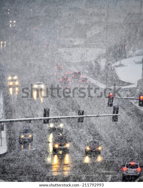 Snowy winter road with several cars driving on\
roadway with traffic\
lights