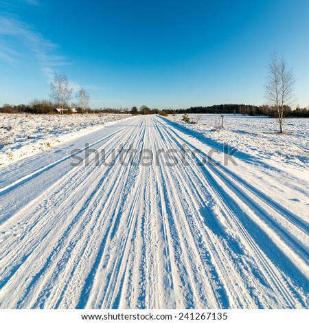 snowy winter road with tire markings and blue sky - square image