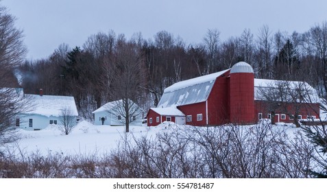 Snowy Winter Scene Of A Farm House With Smoke Rising From Chimney  With A Large Red Barn 
