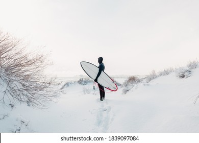 Snowy winter and surfer with surfboard. Winter beach and surfer in wetsuit. - Powered by Shutterstock