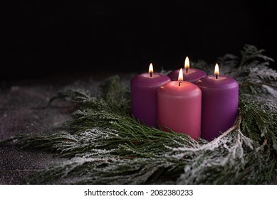 Una corona de nieve con cuatro velas ardientes de advenimiento morado sobre un fondo de madera oscura, tradición católica navideña.