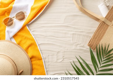 Soak up the sun. Top view of sunbathing essentials: sunglasses, sunhat, beach bag, sunscreen, towel, natural palm leaves. Sandy shore backdrop with an empty space for text or ads - Powered by Shutterstock