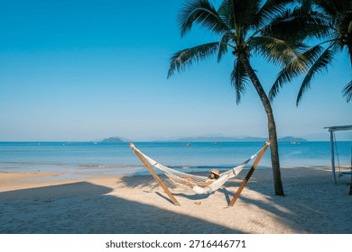 Soaking up the sun while lying in a hammock on the serene beaches of Koh Phayam Island in Thailand. The clear blue sky and gentle waves create a perfect tropical escape.