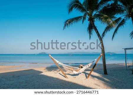 Soaking up the sun while lying in a hammock on the serene beaches of Koh Phayam Island in Thailand. The clear blue sky and gentle waves create a perfect tropical escape.