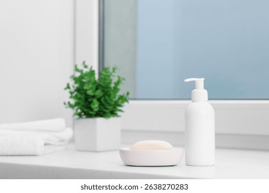 Soap bar, bottle of cosmetic product, towels and floral decor on white window sill indoors