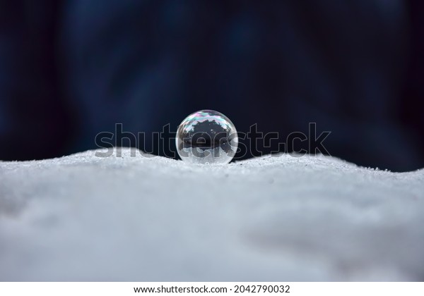 Soap bubble frozen in winter in the frost.\
Transparent ball made of liquid. The background is divided into\
dark and light