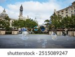 Soap bubbles floating across City Hall square with Communication Palace on the background, evening at Valencia, Spain