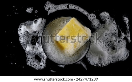 Soap foam with bubbles, porcelain bowl and yellow sponge, washing dishes isolated on black, top view	