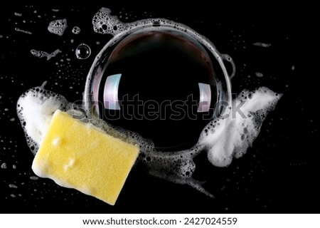 Soap foam with bubbles and yellow sponge isolated on black, top view