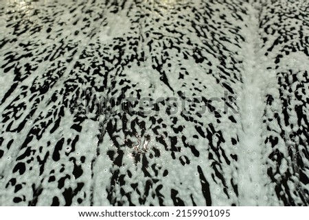 Soap foam on car. Texture of white foam on black car. Washing of transport. Washing agent on surface.