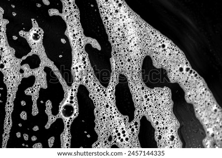 Soap suds create a bubbly texture on the surface. Detergent helps dissolve grease and dirt on dishes. The black plate contrasts and highlights the soap suds.