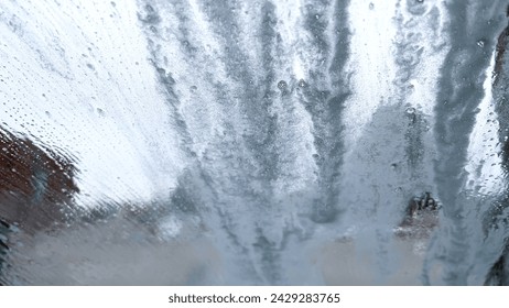 Soapy windshield view from inside a car during an automatic wash cycle, with the foam obscuring the outside.