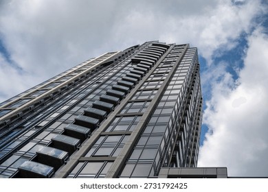 Soaring glass skyscraper façade viewed from below, emphasizing vertical architecture against a dramatic, cloudy blue sky. Modern urban scale.