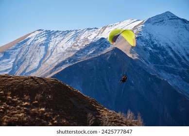 Soaring gracefully in the clear sky, a bright paraglider floats over the majestic snowy mountain peaks.