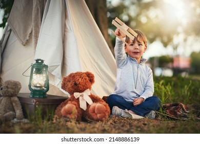 Soaring high above the clouds. Shot of a cute little boy playing with a toy airplane while sitting outside his teepee.