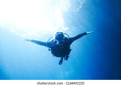 Soaring in the ocean depths. A scuba diver descending towards you with her arms wide open - Copyspace.