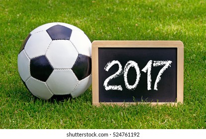 Soccer 2017 - leather ball with wooden chalkboard on green grass background - Powered by Shutterstock