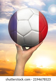 Soccer ball in hand with a depiction of the flag of France against a colorful sky - Shutterstock ID 2194678523