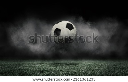 Soccer ball jumping on green grass of football field isolated on dark background with smoke. Concept of sport, art, energy, power. Creative collage. World cup concept. Unfocus effect