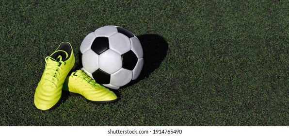 Soccer Ball And Kids Soccer Shoes On Green Grassy Field. Junior Football, Active Sport Outdoor Concept. Panoramic Background, Banner For Web, Copy Space