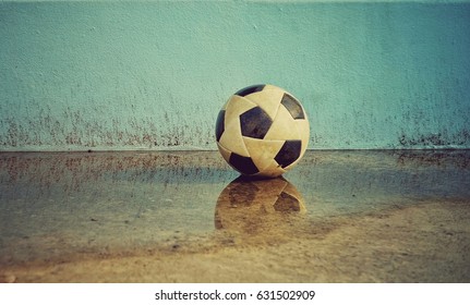 A Soccer Ball On A Cement Floor Reflected In Water.The Soccer Ball On A Cement Wall Background Is A Wall. The Old Soccer Ball Rests On A Cemented Floor.Blue Wall Background