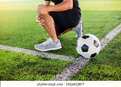 Soccer ball on green artificial turf with footballer is sitting and catch the knee because of pain, soccer player was injured in the foot with pain during competition or practice. - Powered by Shutterstock