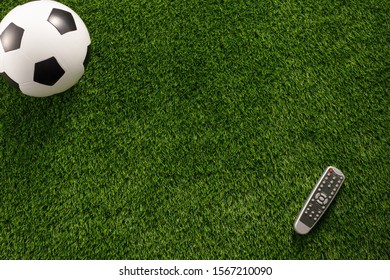 Soccer Ball On A Green Field And A TV Remote Control. Flat Lay Concept Of Football Matches.