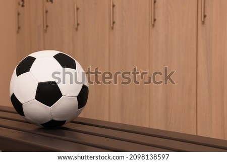 Soccer ball on wooden bench in locker room. Space for text
