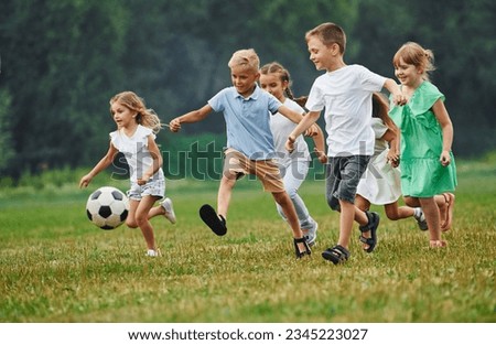 Soccer ball, playing together. Kids are having fun on the field at daytime.
