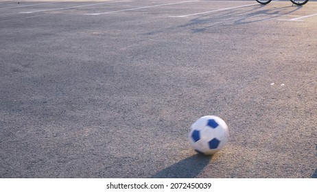 A soccer ball is rolling on the asphalt. Children play with a ball on the road where cars drive. Dangerous ball games on the road.