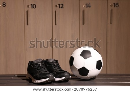 Soccer ball and sneakers on wooden bench in locker room
