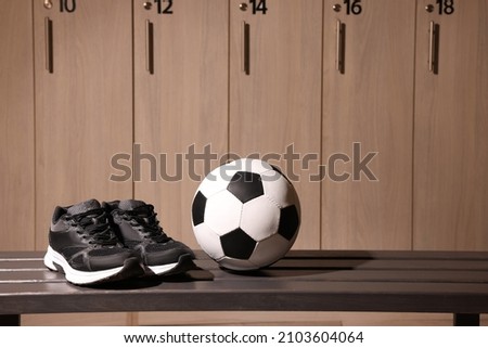 Soccer ball and sneakers on wooden bench in locker room