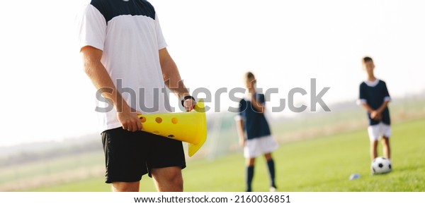 Soccer coach holding\
yellow training cone during oudoor  practice session. Coaching\
junior level soccer team