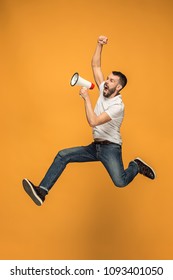 Soccer fan jumping on orange background. The young man as football fan with megaphone isolated on orange studio. Support concept. Human emotions, facial expression concepts.