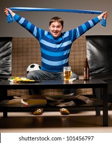 Soccer Fan Is Sitting On Sofa With Scarf In Hands With Beer At Home