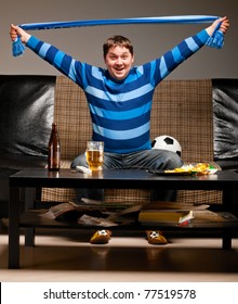 Soccer Fan Is Sitting On Sofa With Scarf In Hands With Beer At Home