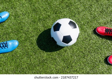 Soccer football background. Soccer ball and two pair of football sports shoes on artificial turf soccer field with shadow from football goal net on sunny day outdoors. Top view