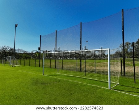 A soccer or football goal is seen on a green grass field with freshly painting white lines under a blue sky with no clouds.  Youth or college sports for training, inspiration, and dreams.