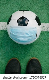 Soccer Football With Surgical Face Mask On Middle Line Of Artifiical Turf Field, Ready For Kick Off, Symbol Image For Sports During The Corona Covid-19 Pandemic In 2020